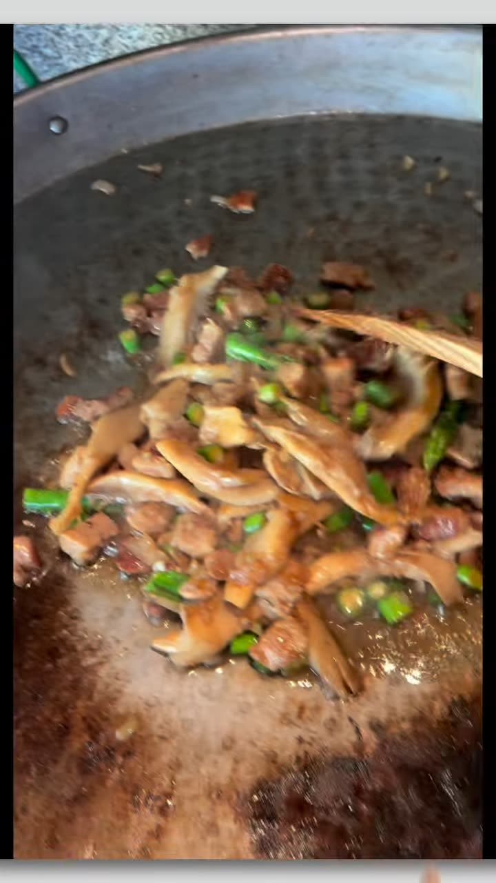 El sofrito de carne y espárragos moviéndose en la paellera con una cuchara de madera