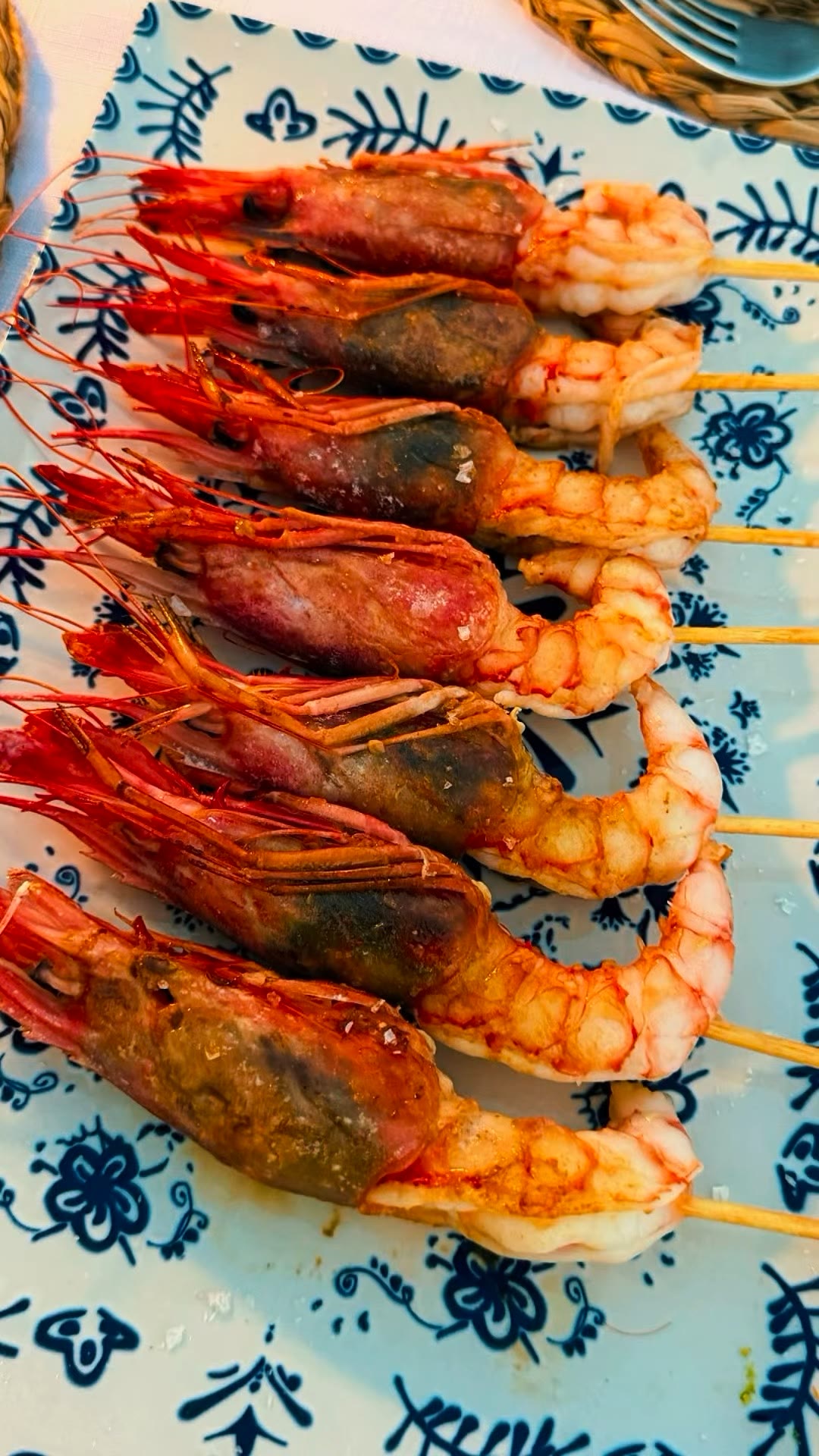 Brochetas de gamba recién hechas, alineadas sobre una bandeja de cerámica azul y blanca