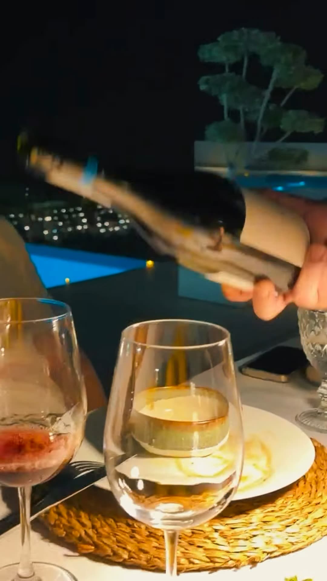 Sirviendo vino blanco en dos copas de noche, con las luces de la costa desenfocadas al fondo